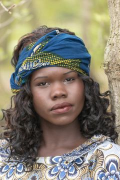Vrouw met een blauwe hoofddoek bij een boomstam, buiten